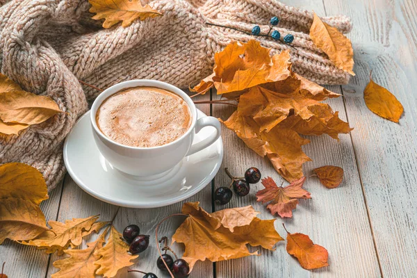 A cup of coffee on an autumn morning against the background of foliage and a sweater. Side view, copy space.