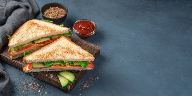 Koyu mavi arka planda tahta bir tahtada iki jambonlu ve peynirli sandviç..