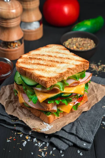 Panino alla griglia con prosciutto, formaggio e verdure fresche su fondo scuro con ingredienti e spezie. — Foto Stock