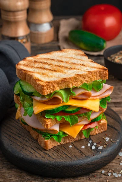A large sandwich with ham, cheese, tomatoes and cucumber close-up. Side view. — Stock Photo, Image