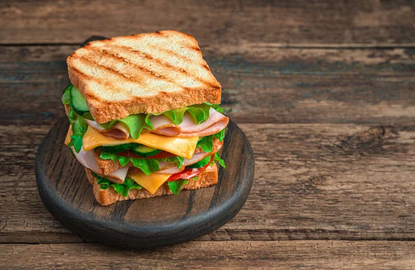 Sanduíche de clube com presunto, queijo, legumes e torradas grelhadas em um fundo marrom de madeira. — Fotografia de Stock