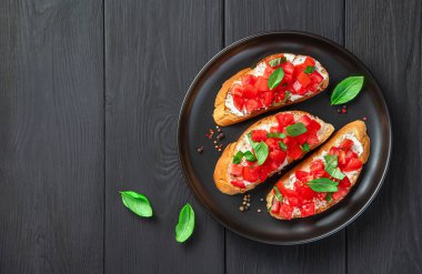 Geleneksel bruschetta domatesli, fesleğenli, peynirli ve tereyağlı siyah ahşap arka planda. Domatesli sandviç. İtalyan mezesi..