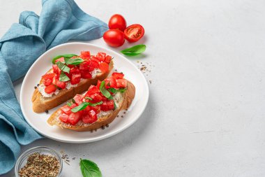 İki kızarmış tost, domatesli, krem peynirli, otlu ve tereyağlı gri arka planda. Geleneksel İtalyan bruschetta..