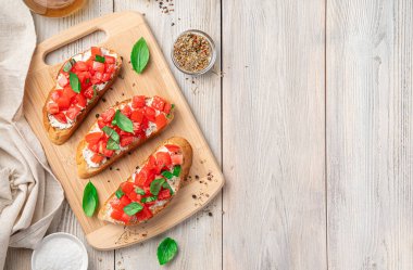 Üç tane domatesli sandviç, beyaz peynir ve hafif ahşap arka planda otlar. İtalyan, geleneksel bruschetta. Üst görünüm, alanı kopyala.