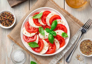 Domatesli bir tabak Caprese salatası, mozzarella ve açık ahşap arka planda fesleğen. Üst görünüm, yakın çekim.