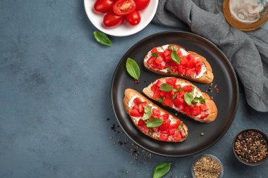 Domatesli İtalyan bruschetta, krem peynir ve koyu gri-mavi arka planda fesleğen. Üst görünüm, alanı kopyala.