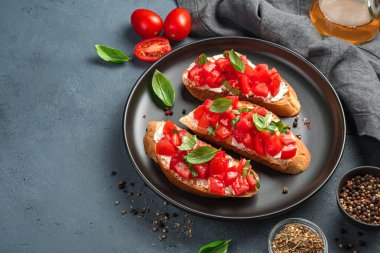 Siyah tabakta domatesli, fesleğenli ve peynirli üç bruschetta. Geleneksel İtalyan yemeği. Yan görünüm.