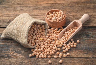 Keten bir torbada çiğ nohut, ahşap bir spatula ve ahşap bir masada bir kase. Yan görünüm.