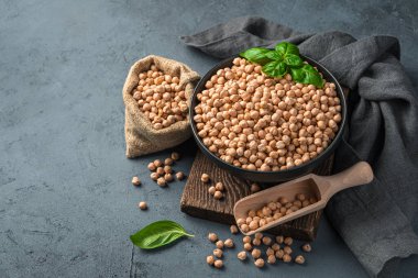 Bir kasede çiğ nohut ve koyu gri-mavi arka planda bir çanta..