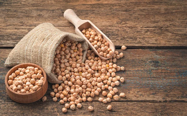 Kuru, keten poşette çiğ nohut, ahşap bir kepçe ve ahşap bir arka planda bir kase..