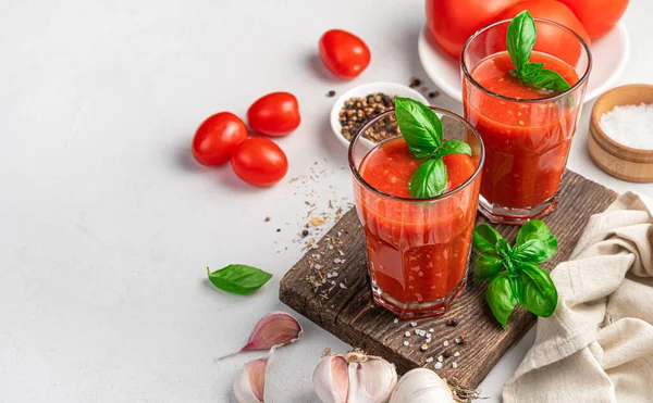 Dos vasos de jugo de tomate sobre un fondo gris con ingredientes. — Foto de Stock