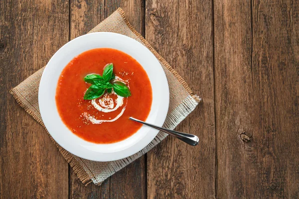 Sopa de tomate com creme e manjericão em uma placa branca em um fundo de madeira. — Fotografia de Stock