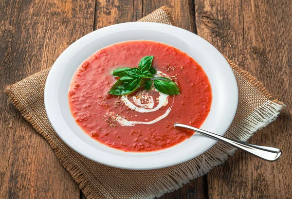 Purê de sopa de tomate com creme e manjericão fresco em um fundo de madeira. — Fotografia de Stock