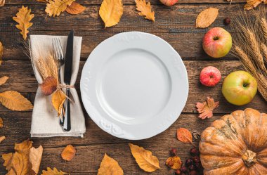 Balkabağı, elma ve sonbahar yapraklarıyla süslü arka planda peçeteli beyaz bir tabak..