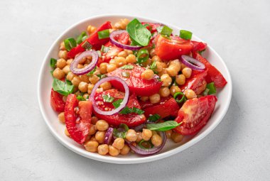 Nohut salatası, domates, taze ot, susam tohumu ve gri arka planda zeytinyağı. Yan görünüm, yakın plan.