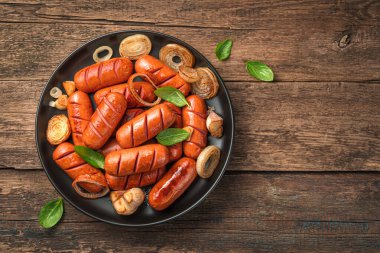 Ahşap arka planda siyah bir tabakta fesleğenli kızarmış sosis. Üst görünüm, alanı kopyala.