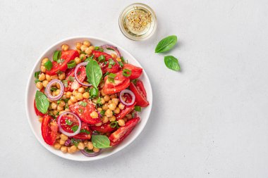 Açık gri arka planda nohut, domates, fesleğen ve susamlı salata..