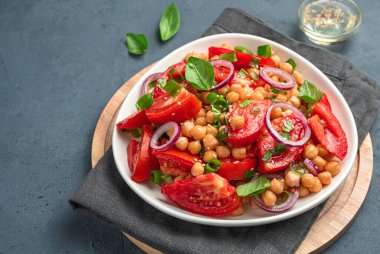 Sağlıklı sebze salatası, nohut, domates ve koyu arkaplanda taze otlar..