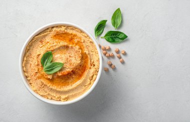 Gri arka planda zeytinyağı, kırmızı biber ve fesleğenli geleneksel humus..