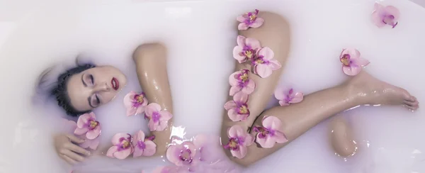 Blonde young model girl in a milk tank with red flowers — Stock Photo, Image