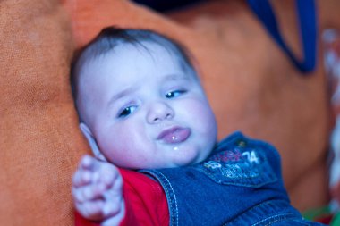 Yeni doğmuş güzel bir bebek, kot tulumuyla kanepede oturuyor. Yüksek kalite fotoğraf