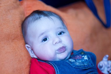 Yeni doğmuş güzel bir bebek, kot tulumuyla kanepede oturuyor. Yüksek kalite fotoğraf