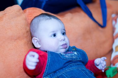 Yeni doğmuş güzel bir bebek, kot tulumuyla kanepede oturuyor. Yüksek kalite fotoğraf