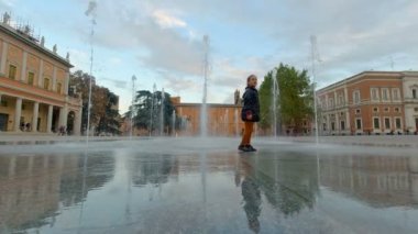 Küçük kız İtalya, Reggio Emilia 'daki Piazza della Vittoria' daki çeşmenin su jetlerini çalıyor. Yüksek kalite 4k görüntü