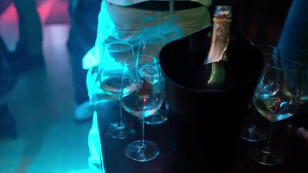 人々が踊っているナイトクラブで眼鏡とスパークリングワインのボトルでテーブルの上を閉じます — ストック動画