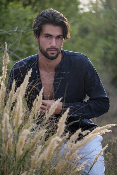 portrait of beautiful dark-haired italian model with light eyes and black shirt with beard in the trees. High quality photo