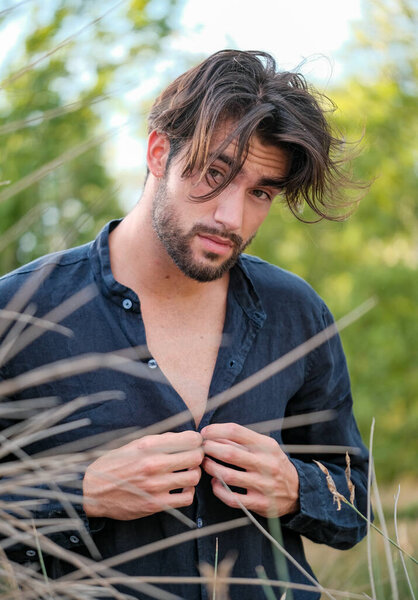 портрет красивой темноволосой итальянской модели со светлыми глазами и черной рубашкой с бородой на деревьях. Высокое качество фото