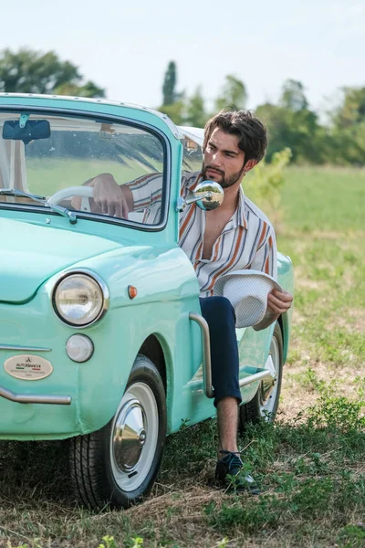 portrait of beautiful dark-haired italian model man with light eyes with beard in an old italian tiffany car. High quality photo