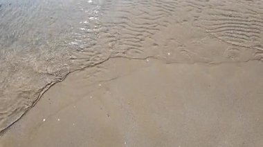 Close-up overhead view of very shallow, clear water retreating from the shore, leaving intricate wave patterns on the wet sand. High quality 4k footage