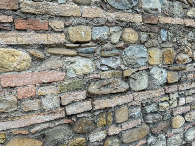 Düzensiz doğal taşlardan ve yıpranmış kırmızı tuğlalardan oluşmuş engebeli, tarihi bir duvarın tam bir iskeleti. Yüksek kalite fotoğraf