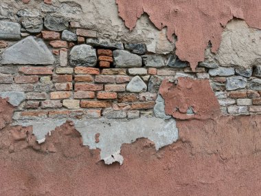 Şiddetli yıpranmış bir duvarın detaylı dokusu, altta yatan sert tuğla ve doğal nehir taşlarını ortaya çıkarmak için kırmızımsı sıva tabakalarının soyulduğu yer. Yüksek kalite fotoğraf