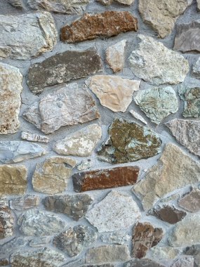 Detaylı, tam kare bir çekim, çeşitli boyutlarda doğal, çok tonlu saha taşları ve görünür havan topu eklemleriyle inşa edilmiş taş bir duvarın engebeli, düzensiz dokusunu sergiliyor. Yüksek kalite fotoğraf