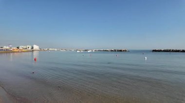 Adriyatik Denizi 'nin Cattolica' daki sakin ve geniş bir fotoğrafı, açık mavi bir gökyüzünün altında açık denize geçiş yolunu tanımlayan iki insan yapımı kaya dalgası içeriyor. Yüksek kalite 4k görüntü