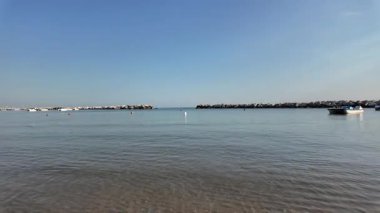 Adriyatik Denizi 'nin Cattolica' daki sakin ve geniş bir fotoğrafı, açık mavi bir gökyüzünün altında açık denize geçiş yolunu tanımlayan iki insan yapımı kaya dalgası içeriyor. Yüksek kalite 4k görüntü