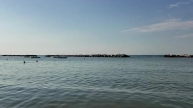 Adriyatik Denizi 'nin Cattolica' daki sakin ve geniş bir fotoğrafı, açık mavi bir gökyüzünün altında açık denize geçiş yolunu tanımlayan iki insan yapımı kaya dalgası içeriyor. Yüksek kalite 4k görüntü