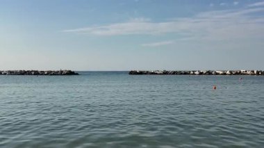 Adriyatik Denizi 'nin Cattolica' daki sakin ve geniş bir fotoğrafı, açık mavi bir gökyüzünün altında açık denize geçiş yolunu tanımlayan iki insan yapımı kaya dalgası içeriyor. Yüksek kalite 4k görüntü