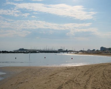 Cattolica 'da sakin bir Adriyatik kıyı şeridi yumuşak dalgalar, kumlu plajlar ve yumuşak bir yaz gökyüzü altında uzak binalar. Yüksek kalite fotoğraf