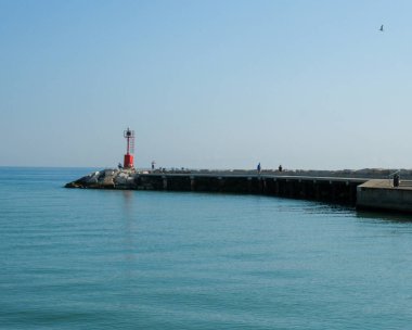 Cattolica 'da, Adriyatik sularına tepeden bakan bir dalgakıran üzerinde parlak bir yaz gökyüzü altında kırmızı bir deniz feneri. Yüksek kalite fotoğraf