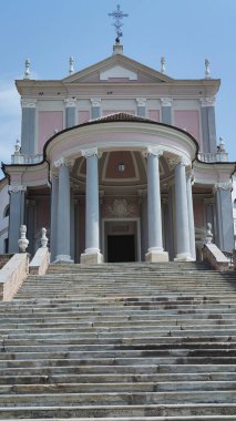 İtalya 'nın Varallo Piedmont bölgesindeki Collegiata di San Gaudenzio' nun önünde geniş bir merdiven ve gün ışığında pembe ve gri bir cepheye karşı kavisli bir kapı var. Yüksek kalite fotoğraf