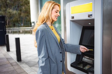 Gülümseyen bir kadın, banka işlemleri için ATM 'ye kredi kartı sokuyor.