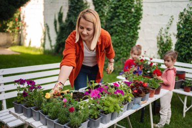 Bir kadın ve iki kız sevinçle çiçek dikiyorlar..