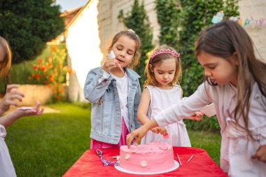 Çocuklar açık havada birlikte pembe bir pasta süsler..