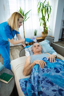 Bakıcı hemşire evde yaşlı bir adamın sıcaklığını ölçer..
