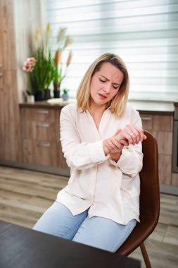 Genç bir kadın şık bir sandalyede oturuyor, bileğini burkuyor..