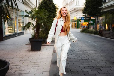 Genç bir kadın neşeli bir Avrupa caddesinde gülüyor ve yürüyor.