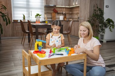 Bir anne ve kızı bir masada eğlenceli bir zanaat seansı düzenler, plastiklerle renkli sanatlar yaratır ve birlikte kaliteli zaman geçirmekten zevk alırlar..